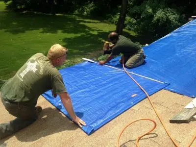 Two men working on a tarp covering the ground.