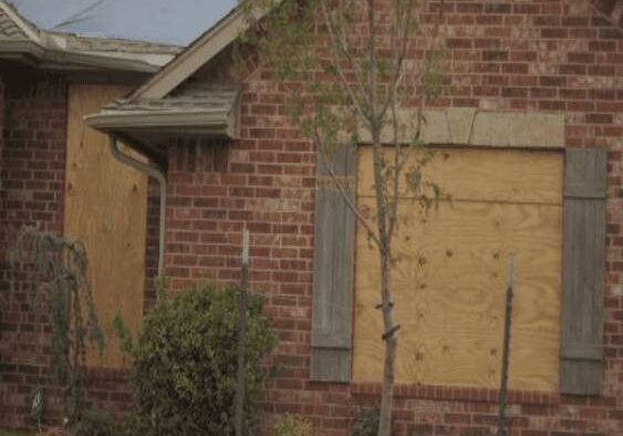 A brick house with boarded up windows and trees.